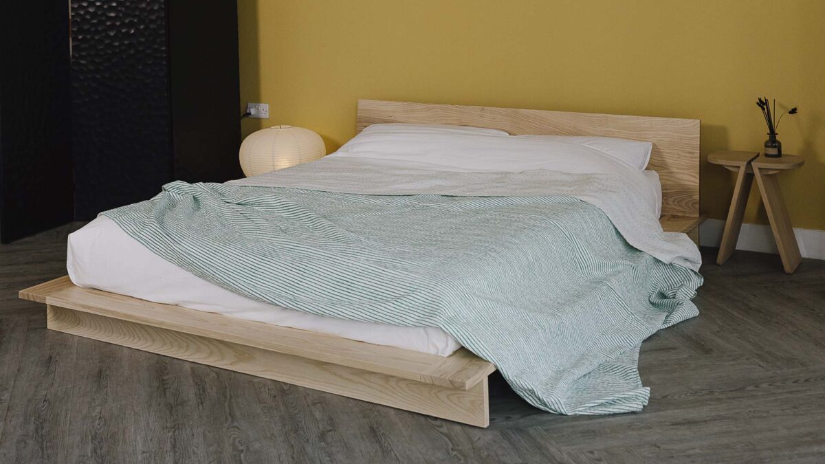 Green Striped bedspread draped over white bed linen on a ash platform bed frame.