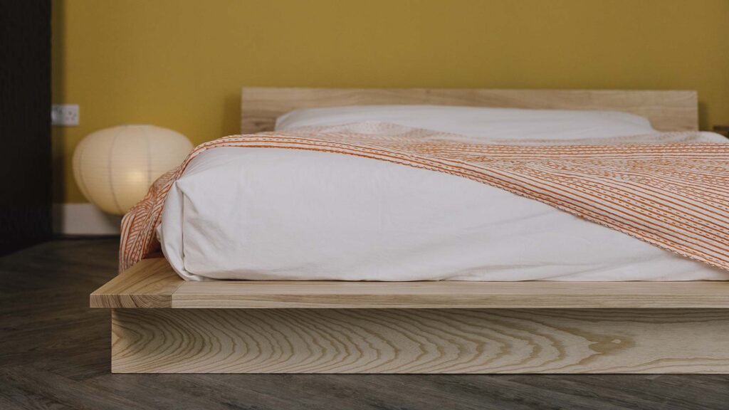 Orange Striped bedspread draped over white bed linen on a ash platform bed frame.