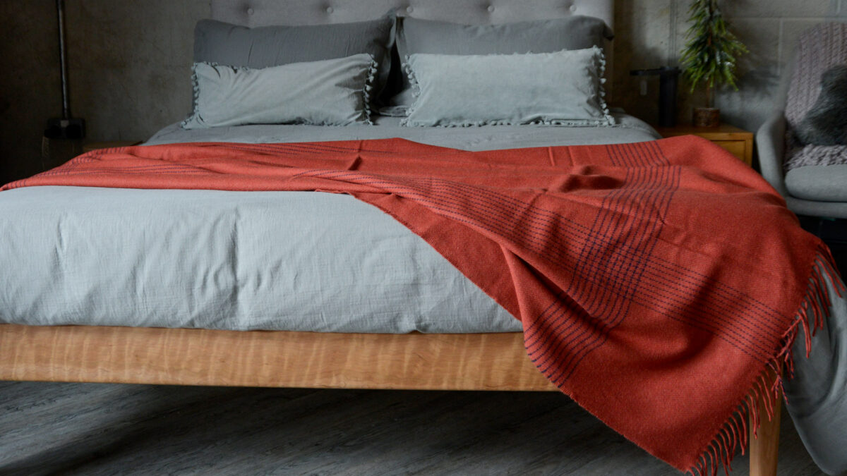 rust red cashmere lambswool throw with navy threads detail shown draped on a kingsize bed