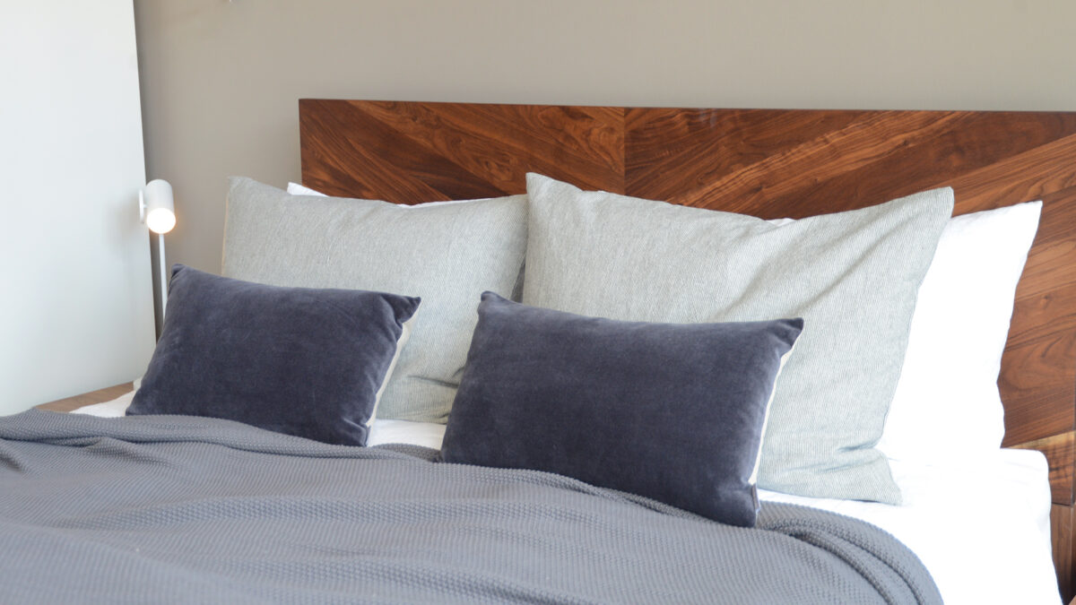 narrow striped large cotton cushions shown on a bed and with smaller velvet cushions