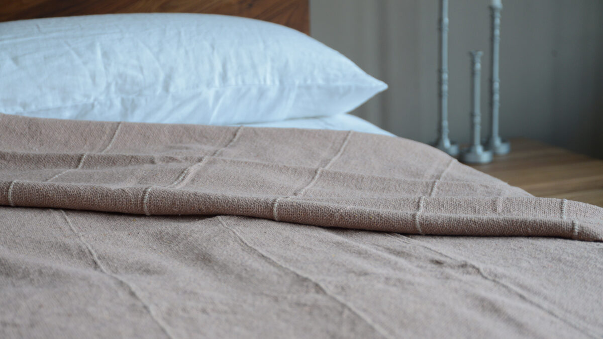 striped and tasselled textured cotton bedspread in blush pink and ivory shown on a bed