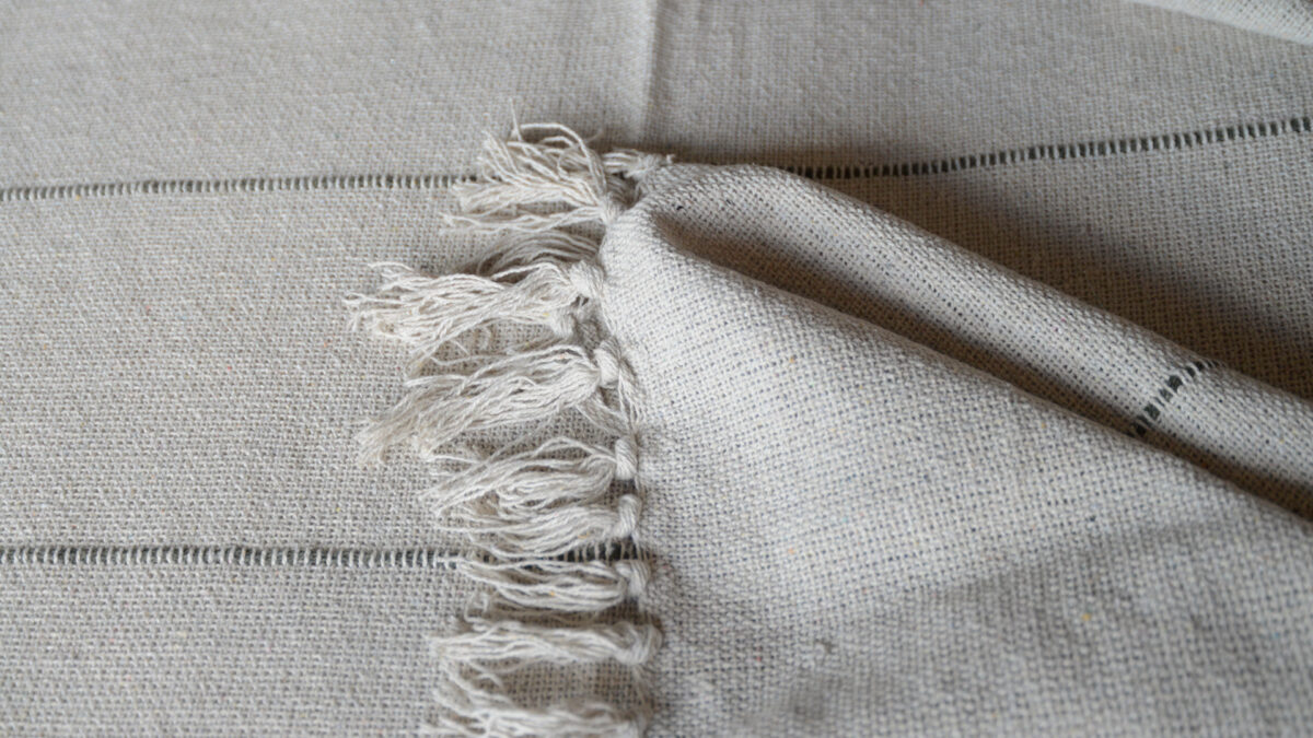 striped and tasselled cotton bedspread in stone and grey shown up close