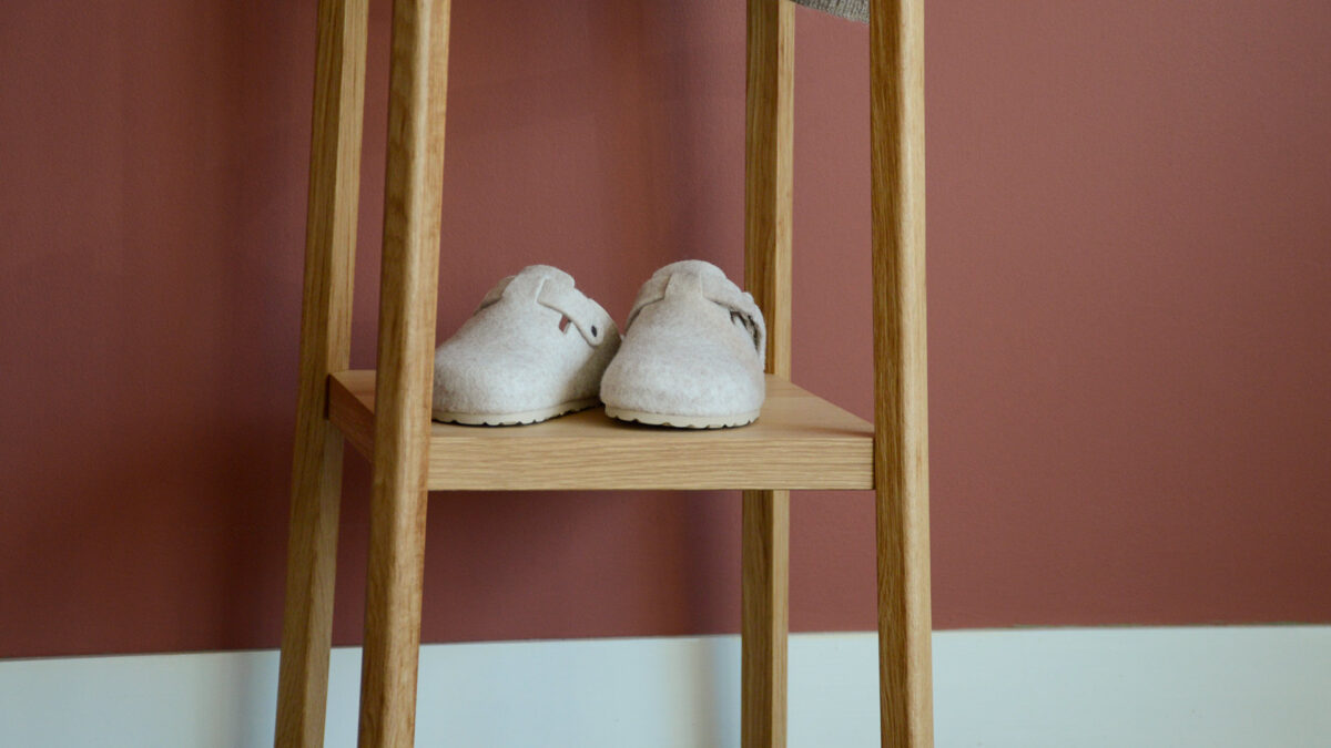 closeup of shelf at base of coat stand. Light grey woollen slippers on shelf.