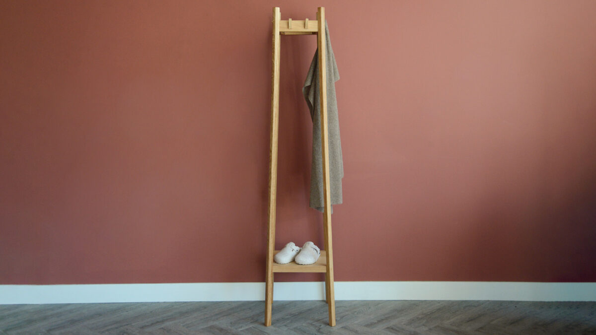Full view of tall coat stand with bottom shelf. Scarf hanging from hook, slippers on shelf.