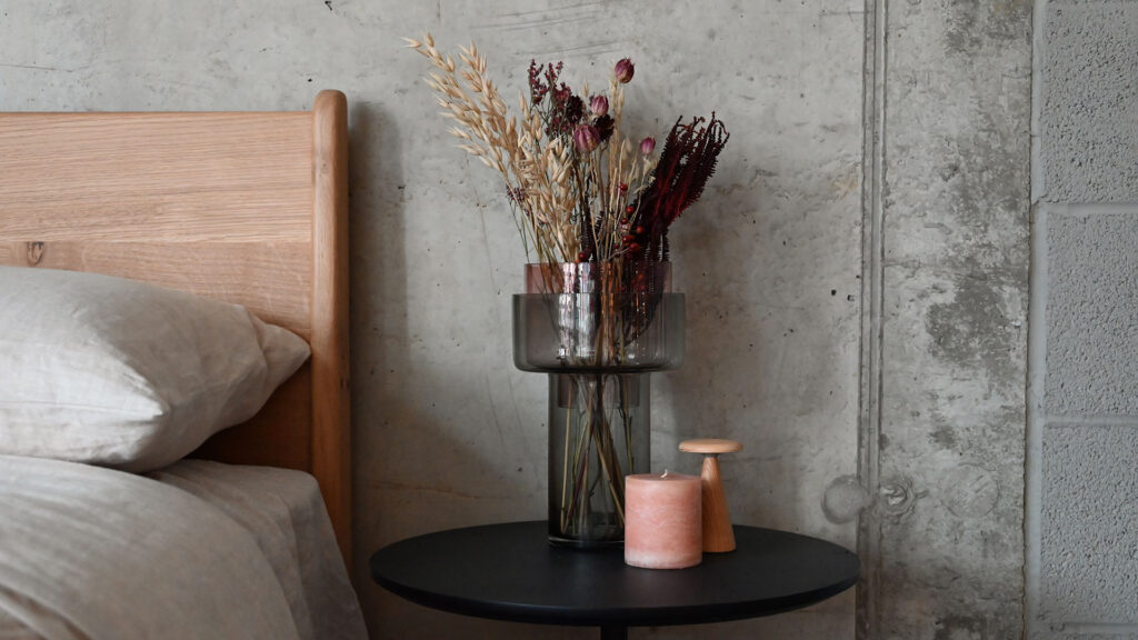Two tone glass vase with removable top section and wide opening. Large bouquet of flowers. On a black round table with a small lamp and candle.