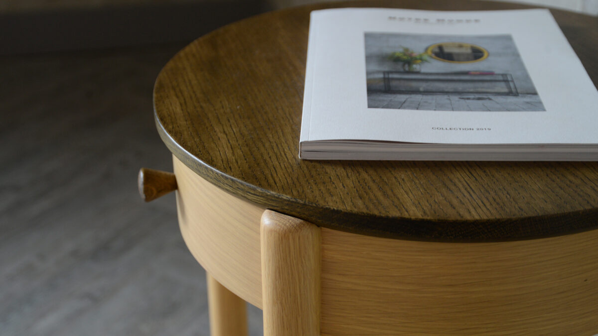 circular bedside table with drawer in a natural oak with a dark stained top