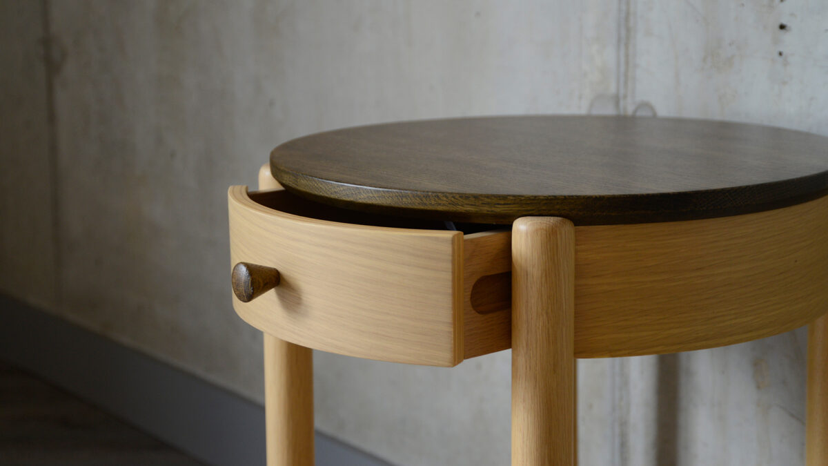 a closer view of the circular dark topped bedside table with drawer open