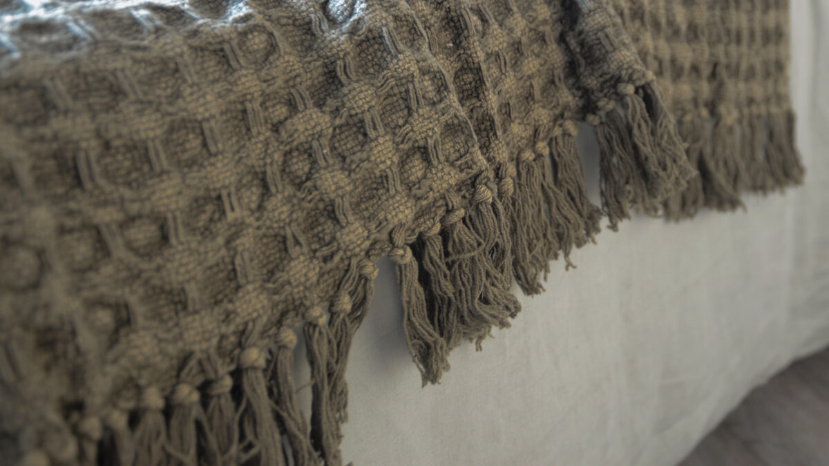 textured weave fringe edged throw in an olive green colour