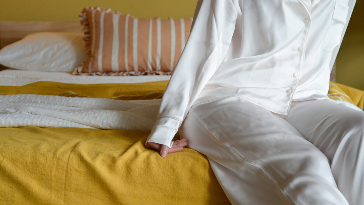 close up of worn white satin pyjamas showing cuff detail, buttons and pocket on the pyjama top.