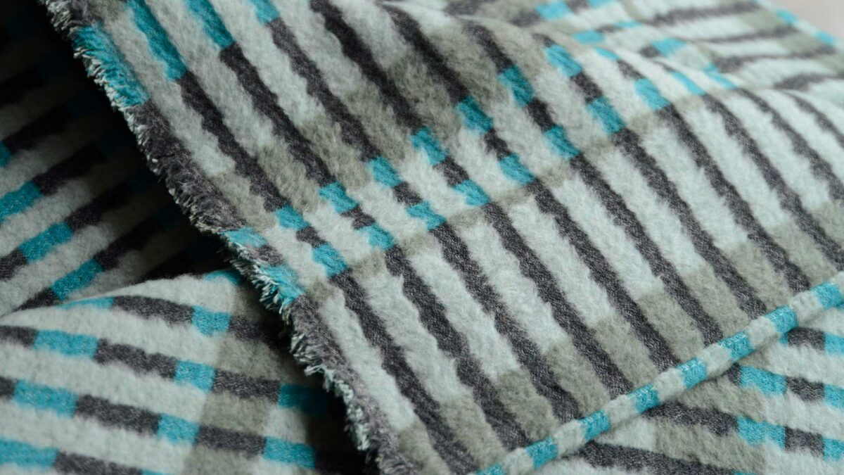 patterened stripey fluffy throw in black and teal tones shown on a bed