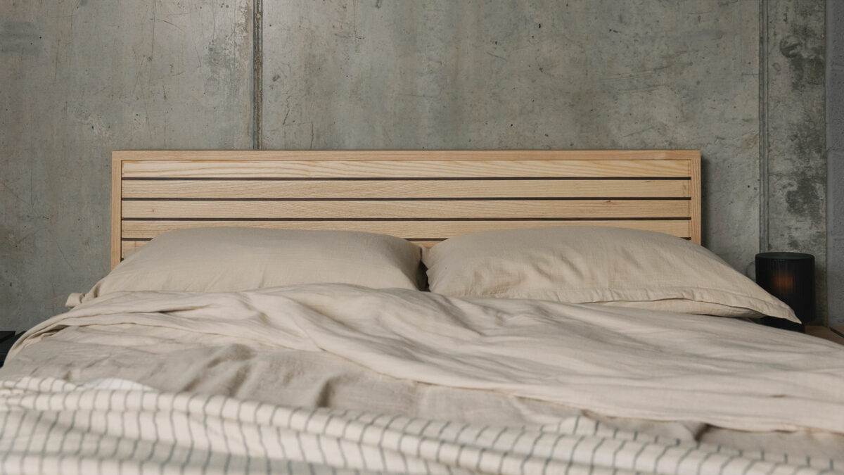 A special edition Leith bed in Ash wood with walnut stripes to the headboard panel shown with stone coloured bedding