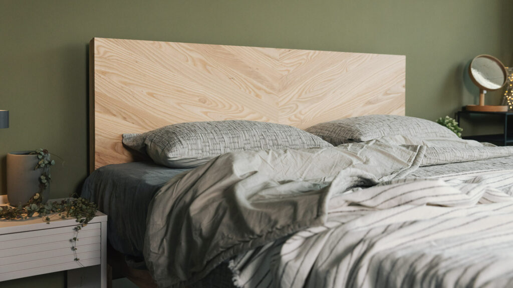 A superking solid Ash Hathersage bed with chevron pattern headboard shown with moss grey bedding