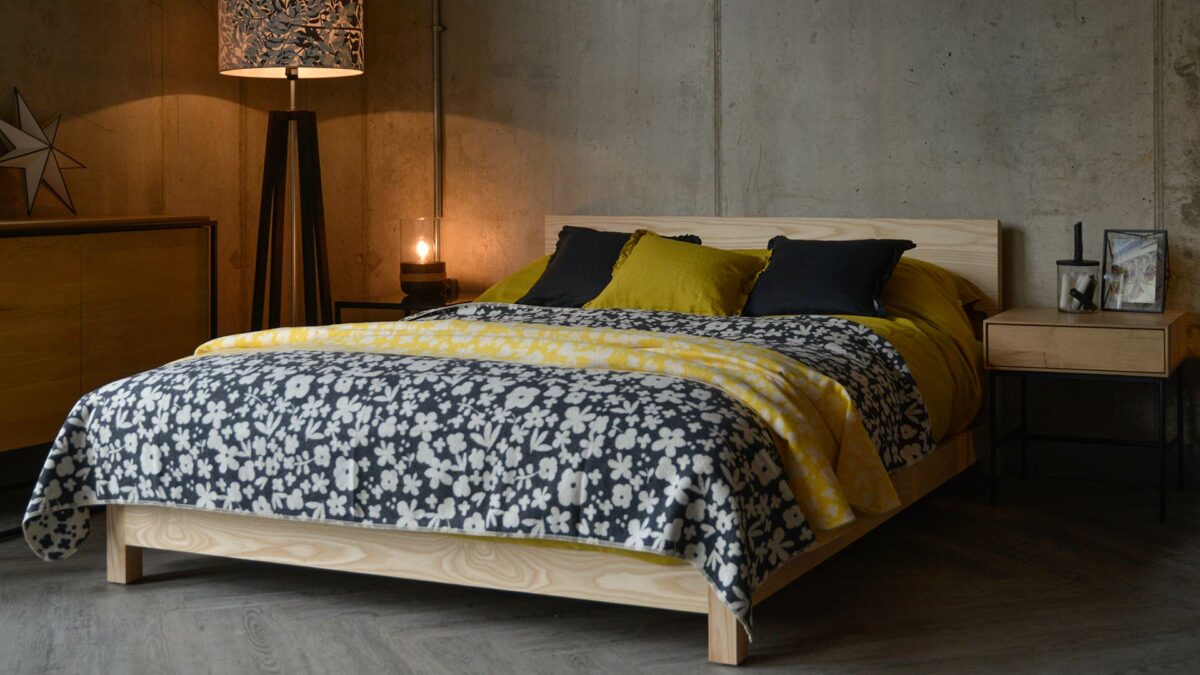 Modern floral Marimekko style cotton rich soft throws in charcoal and yellow shown on Sonora low wooden bed