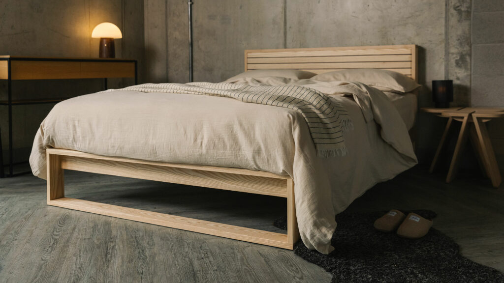 A special edition Leith bed in Ash wood with walnut stripes to the headboard panel shown with stone coloured bedding