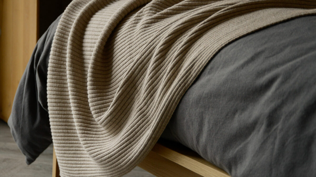 knitted bed runner or pashmina in beige shown draped on a bed