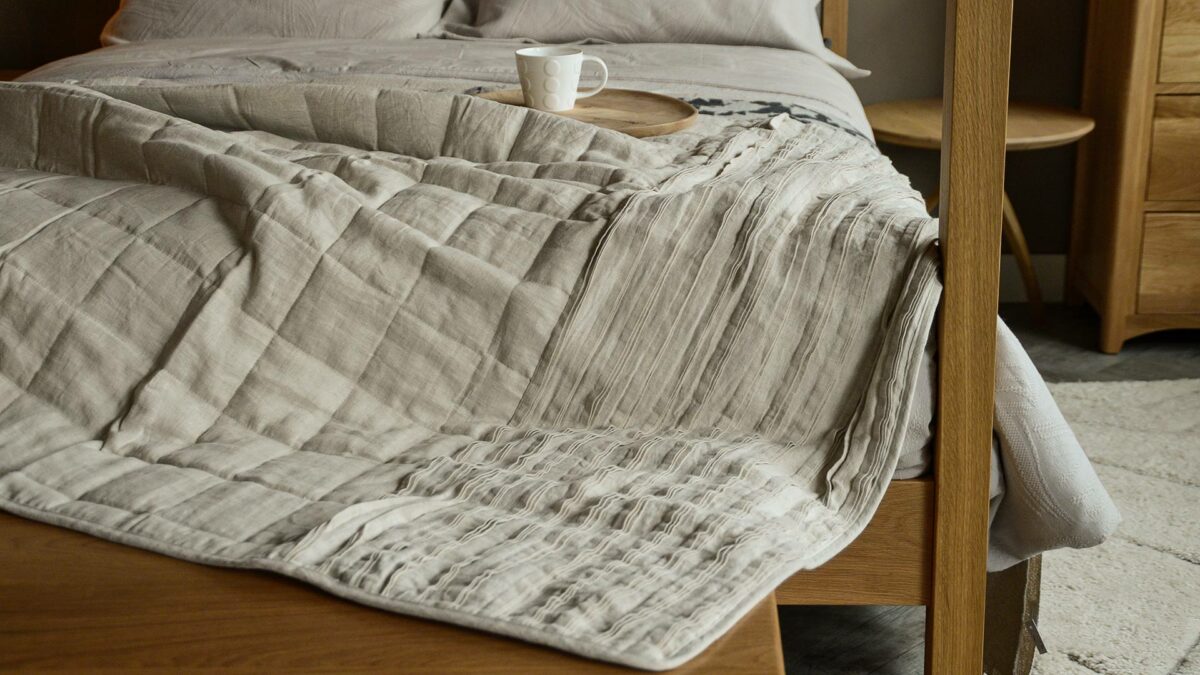 linen quilted ruffle edge throw in beige shown draped on a wooden framed 4 poster bed