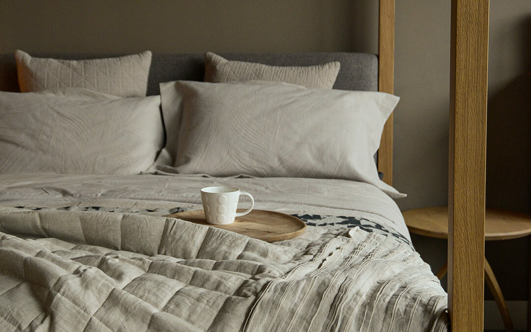 linen quilted ruffle edge throw in beige shown draped on an oak framed 4 poster bed