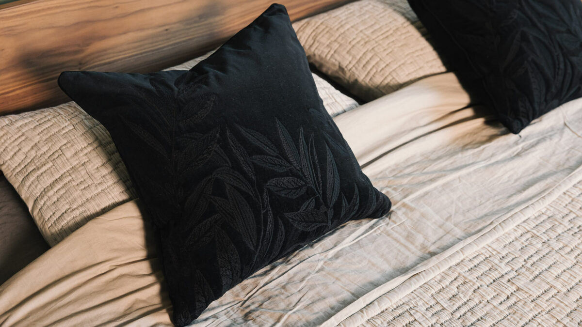 Embroidered black velvet cushions shown on a bed