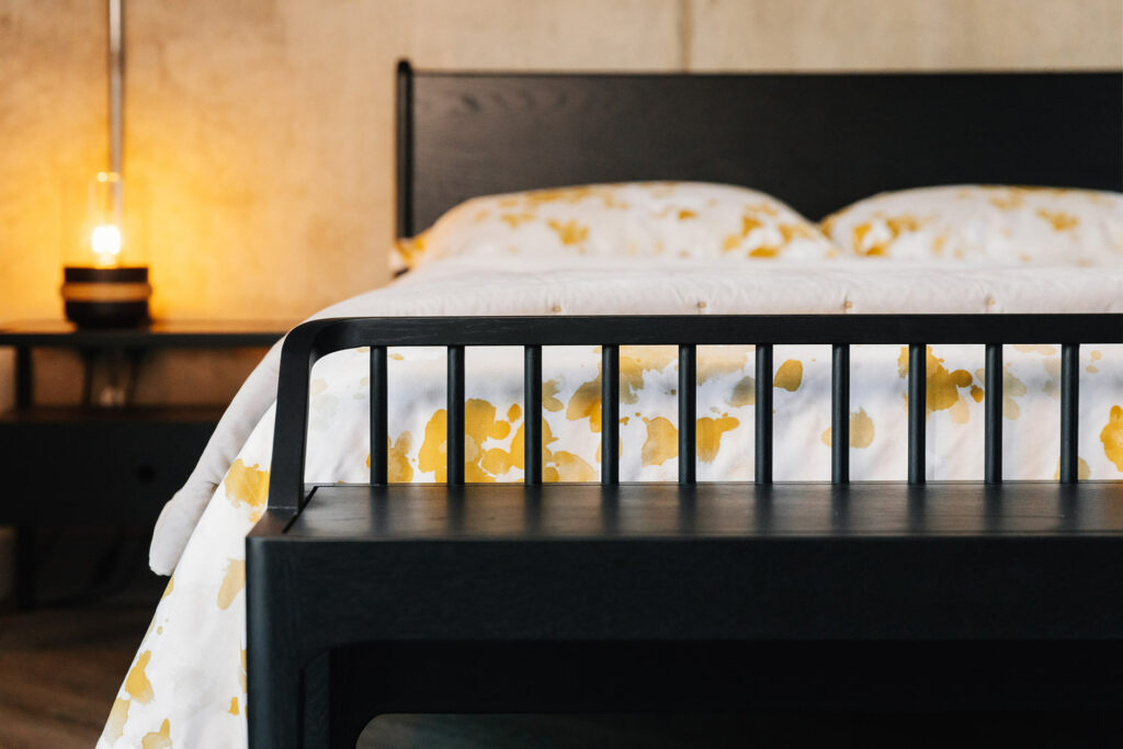 slender spindle bench in black oak shown at the end of a kingsize Camden bed