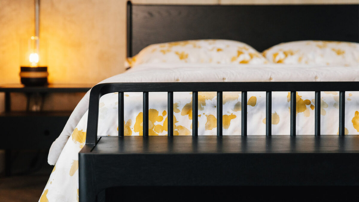 slender spindle bench in black oak shown at the end of a kingsize Camden bed