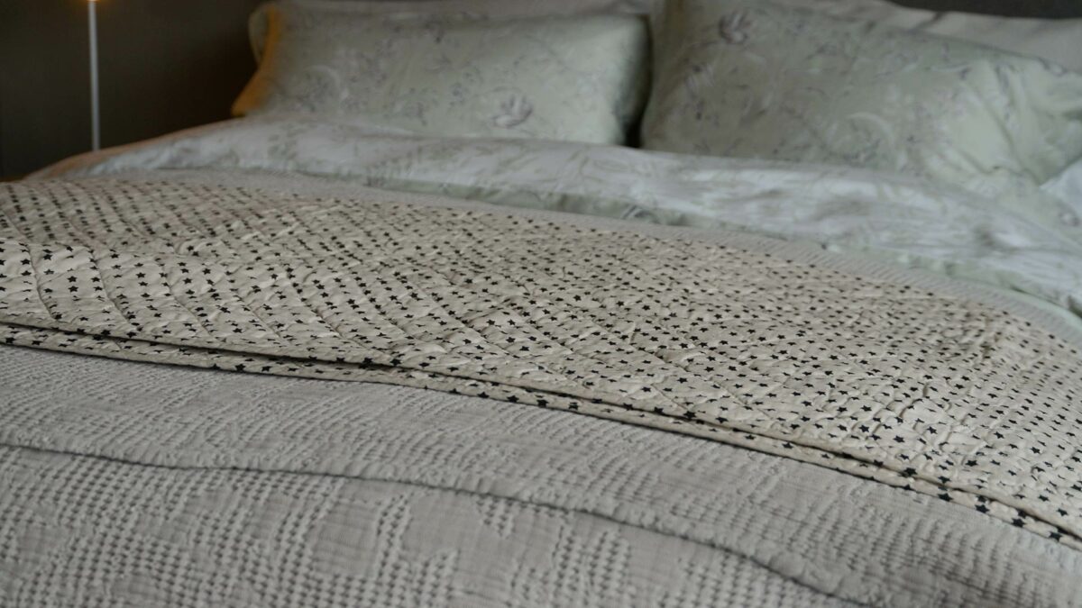 quilted ivory throw with small black stars print shown on a bed