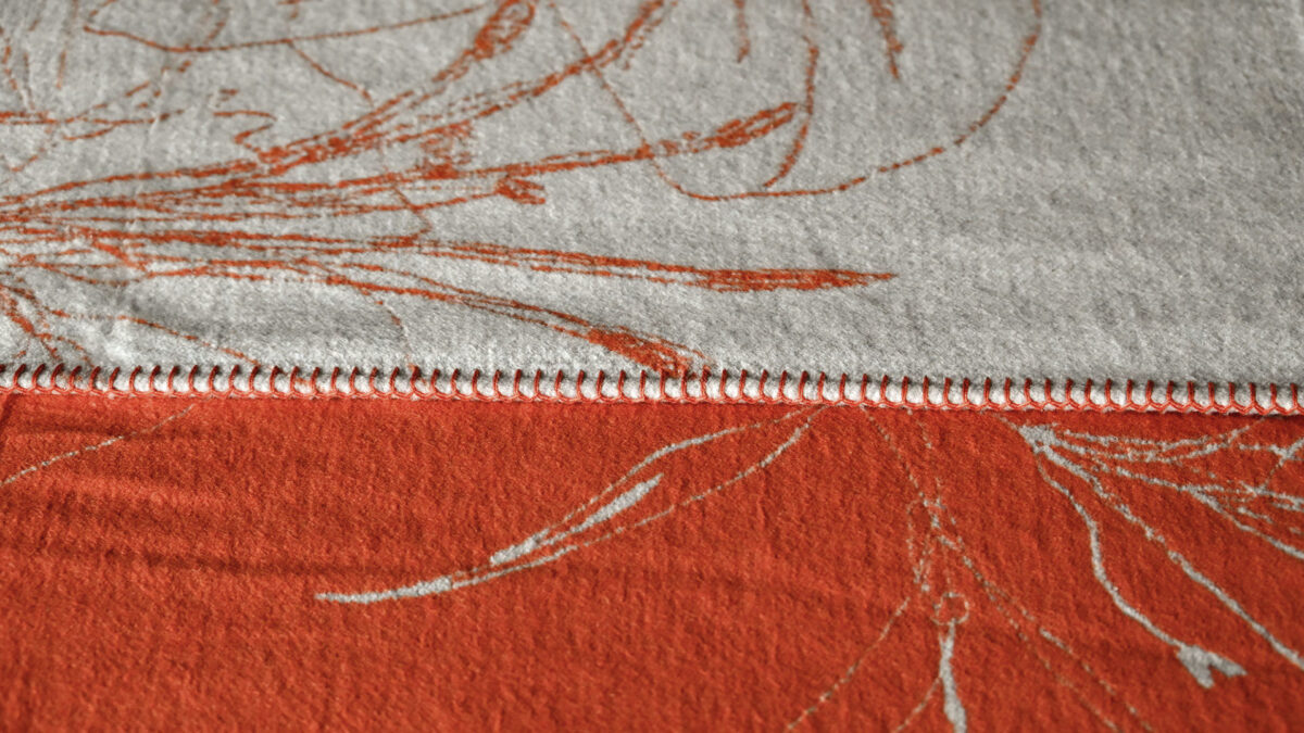 closeup of a reversible throw in orange and ivory. Floral pattern.