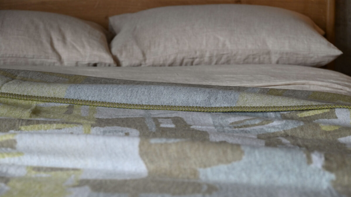 close up of a green and grey throw on a bed, showing the stitching detail on the edges.