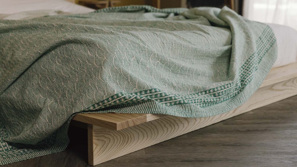 Closeup image of rumpled cotton kantha bedspread with green wave pattern and bold green border.