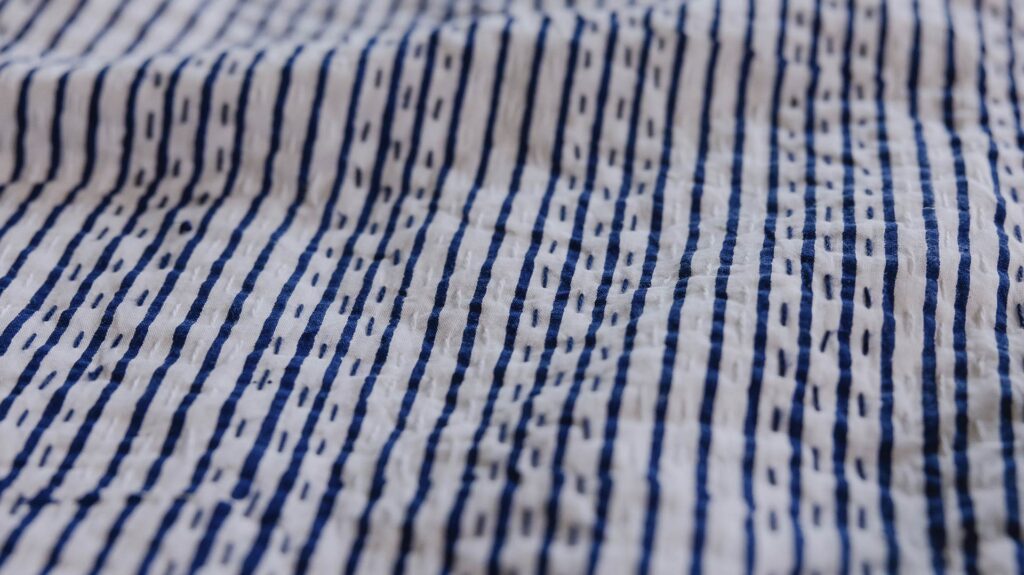 close up of stripe detailing on a blue and white bedspread.