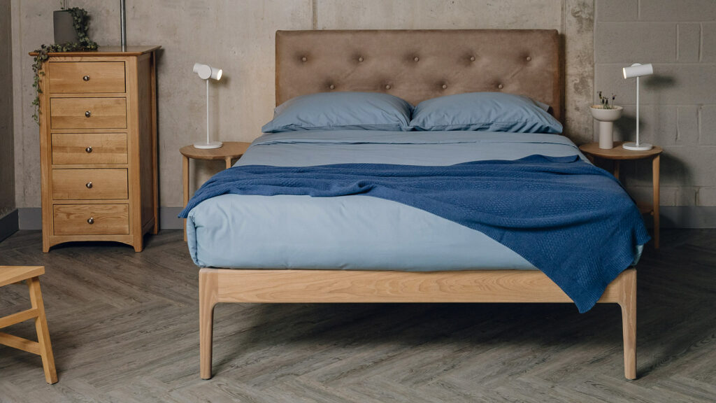 Oak Bloomsbury bed with oiled frame and a headboard upholstered in a faux leather shown with blue bedding