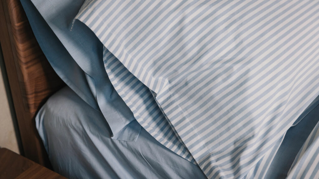 Blue and white striped cotton duvet cover and pillowcase set shown with pale blue chambray bedding