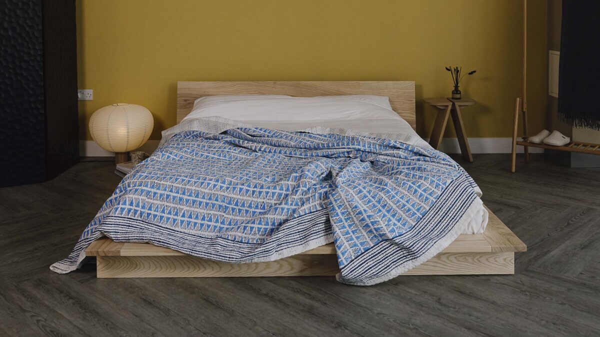 Blue block print bedspread with triangle print and a striped border on an ash bed.