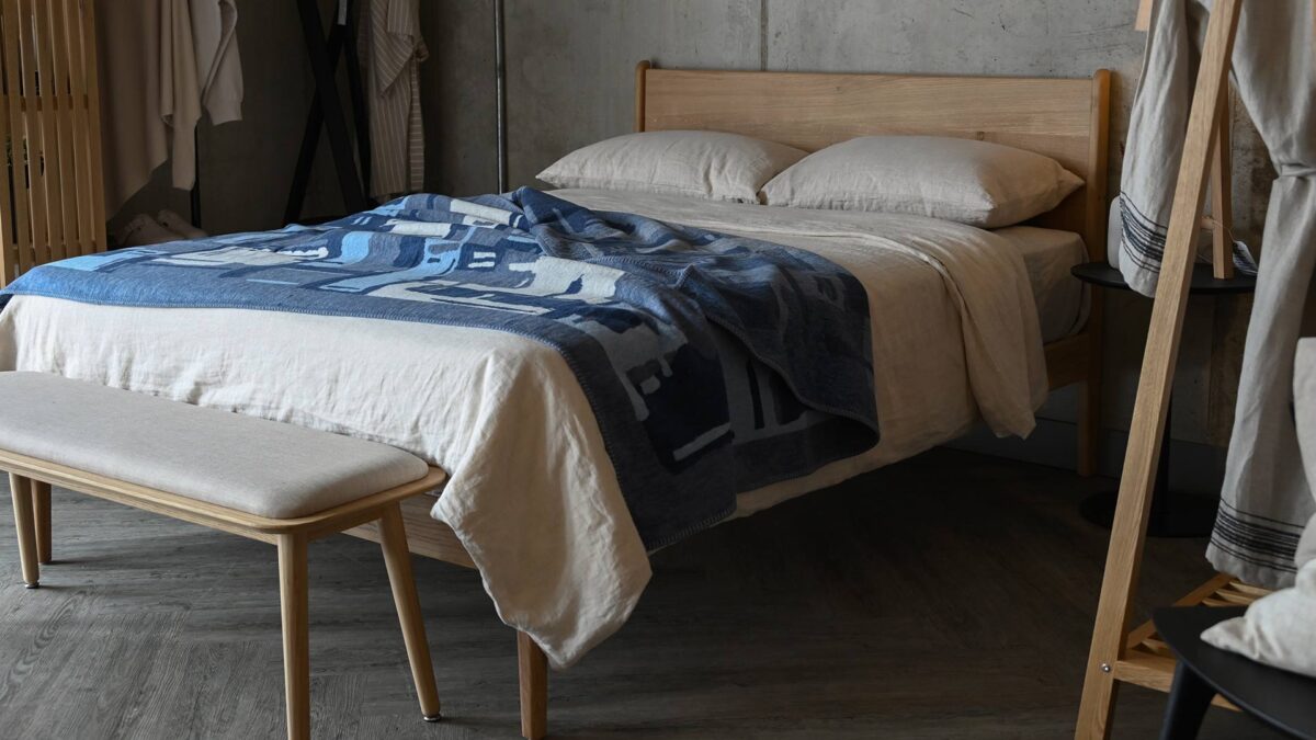 Oak bed with ecru bedding, an abstract patterned blue throw spread on the top.