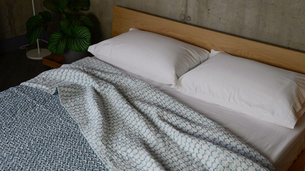 blue and white block printed quilted bedspread shown on a bed with both sides showing