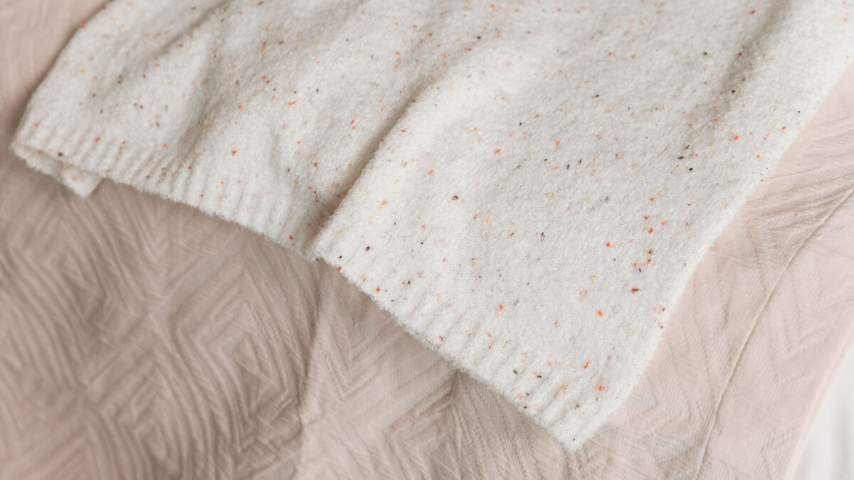 textured blush pink bedspread shown with a knitted speckle throw