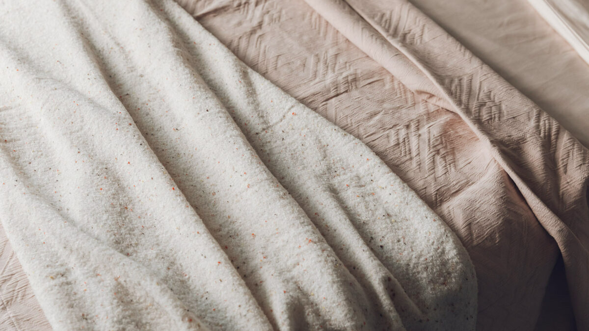 Blush pink textured bedspread shown with knitted speckle throw