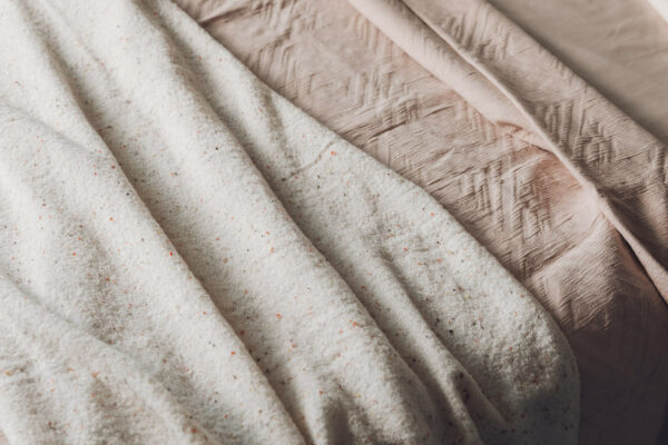 Blush pink textured bedspread shown with knitted speckle throw