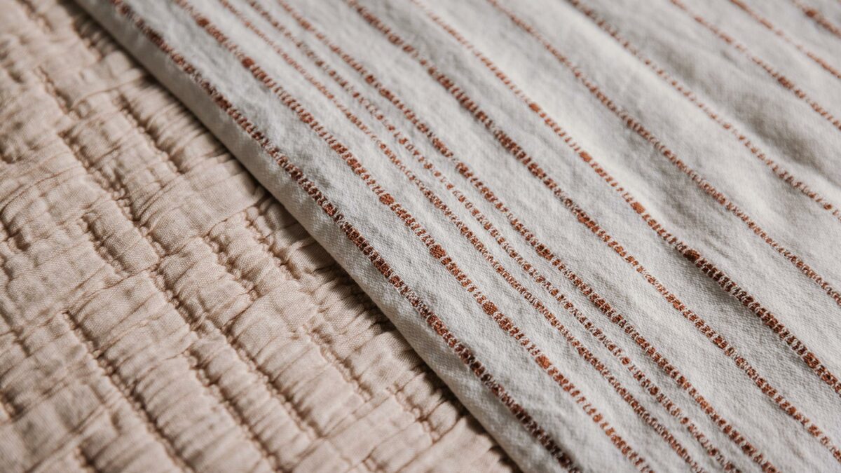 textured bedspread in Blush pink shown with a white and wine striped cotton throw