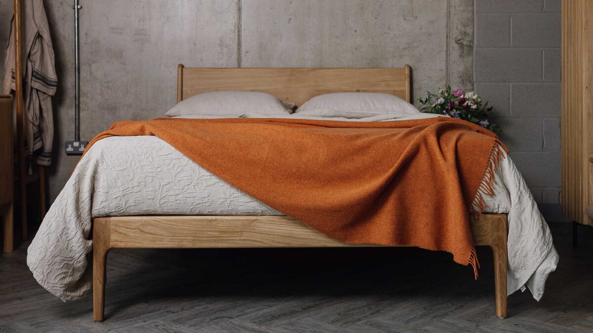 Front view of an English Oak bed with ecru linen and a brunt orange woollen throw with tassels.