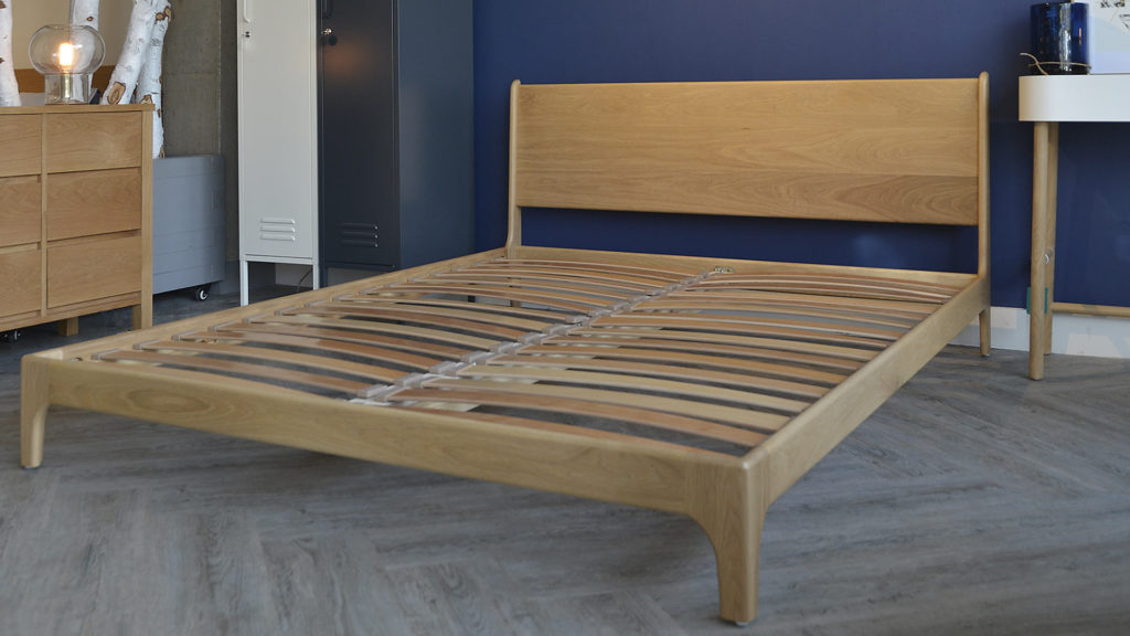 This view of the low wooden Carnaby bed without a mattress shows the curving mid-century style frame and headboard.