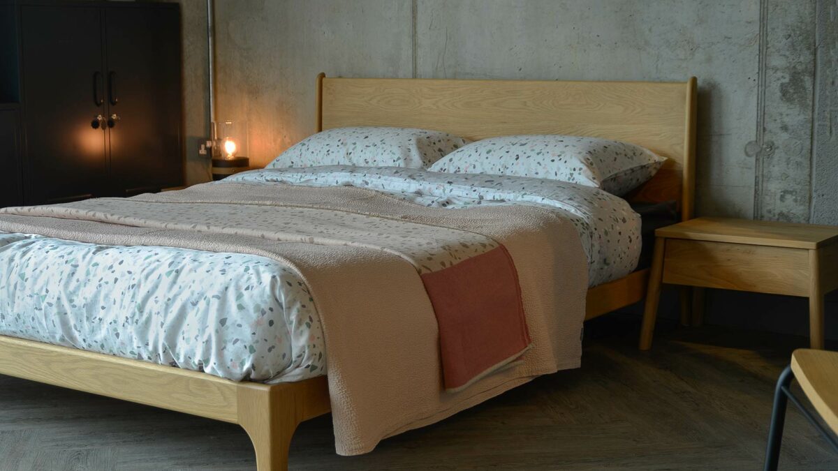 The Carnaby low oak bed from Natural Bed Company is dressed with terrazo print bedding and a cotton bedspread.