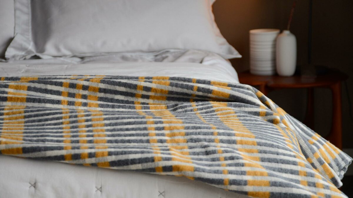 patterened stripey fluffy throw in grey and yellow tones shown on a bed