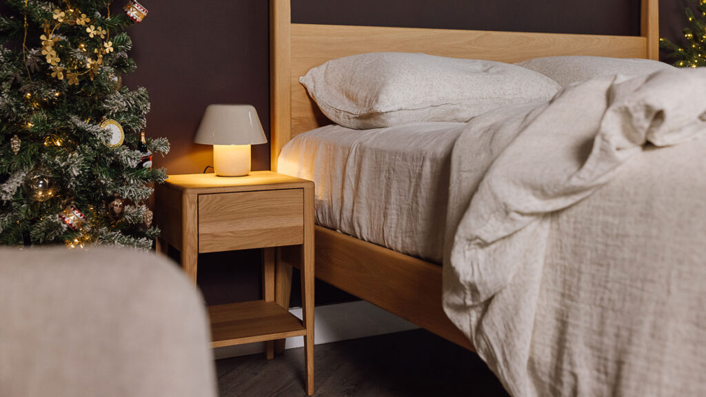 Christmas scene. Oak bedside table with neutral table lamp in focus.