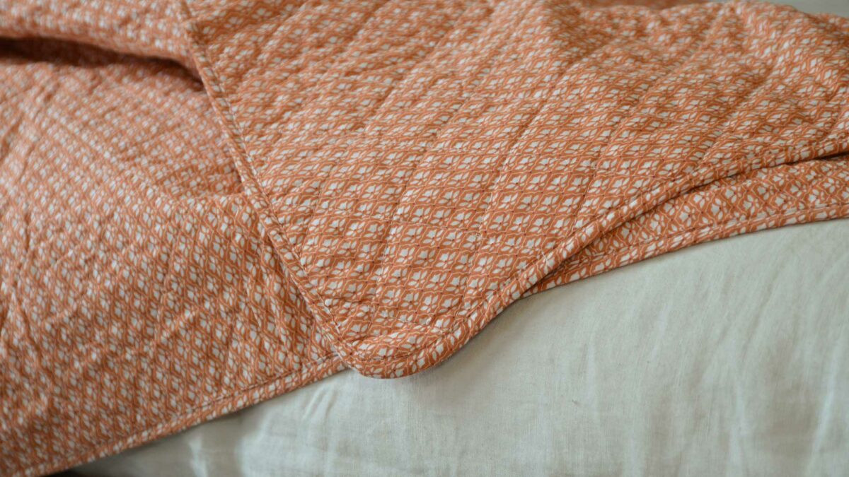 orange quilted throw with a delicate ivory flower pattern, a close-up view