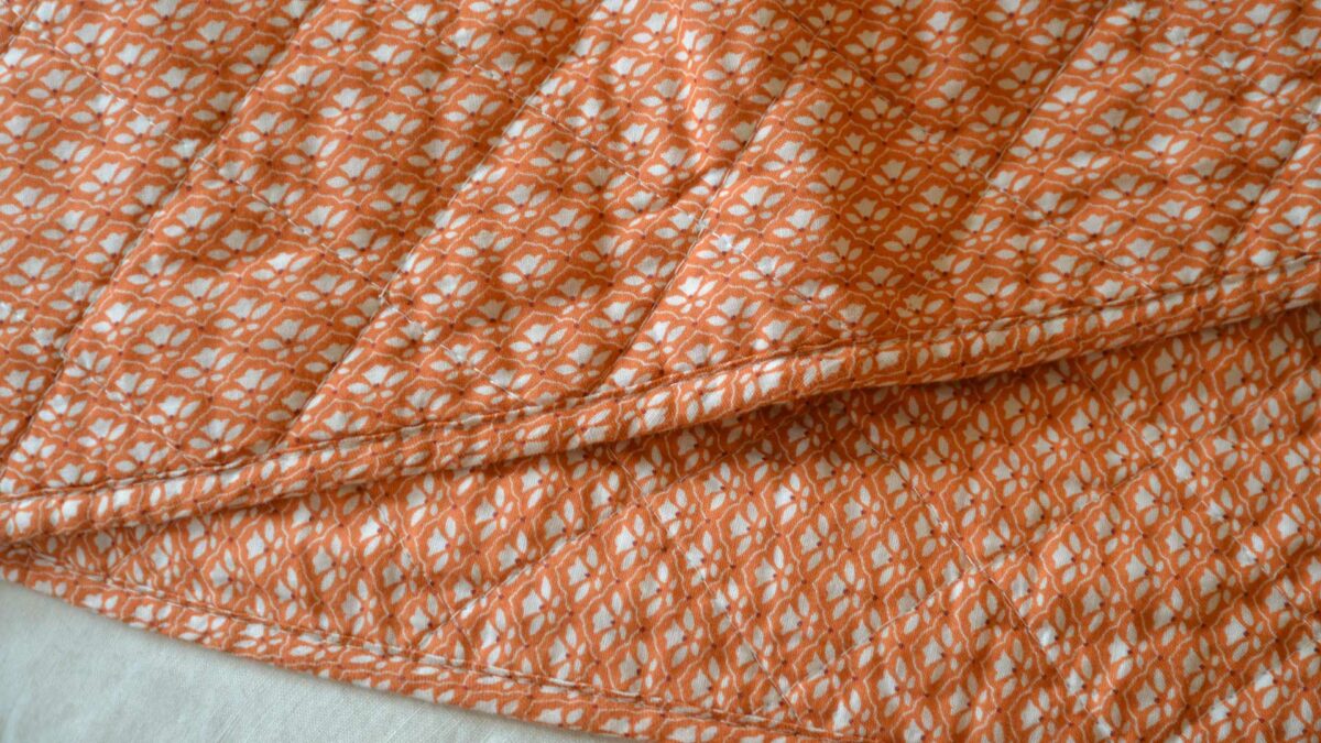 orange quilted throw with a delicate ivory flower pattern, a close-up view
