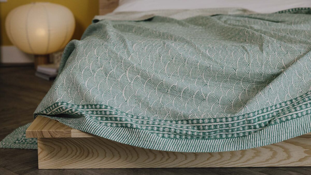 Closeup detail image of the kantha bedspread with green wave pattern and bold, dark green border.