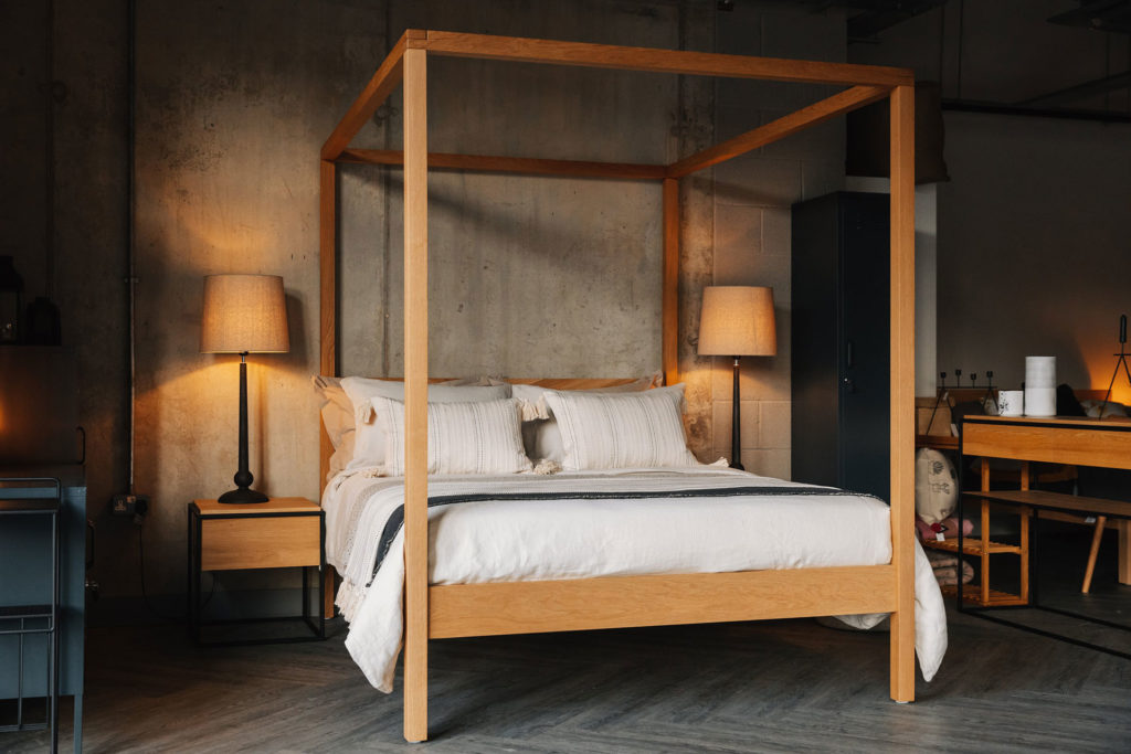 softening an industrial bedroom, luxurious layered bedding and oak wooden 4 Poster bed