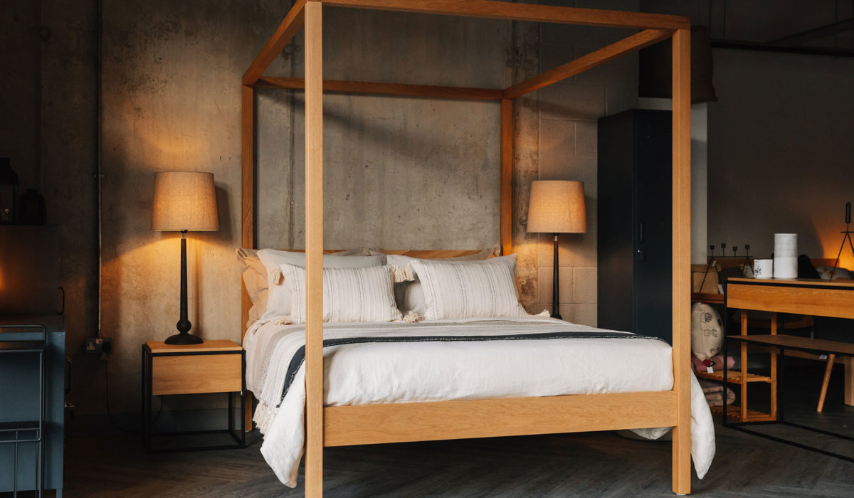 softening an industrial bedroom, luxurious layered bedding and oak wooden 4 Poster bed