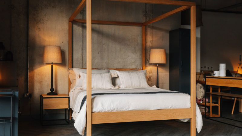 softening an industrial bedroom, luxurious layered bedding and oak wooden 4 Poster bed