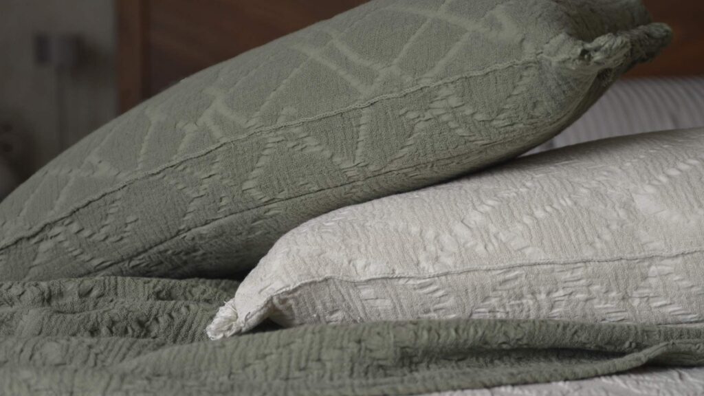 Textured cotton cushions in the colours olive and light ecru, stacked on top of a textured olive throw.